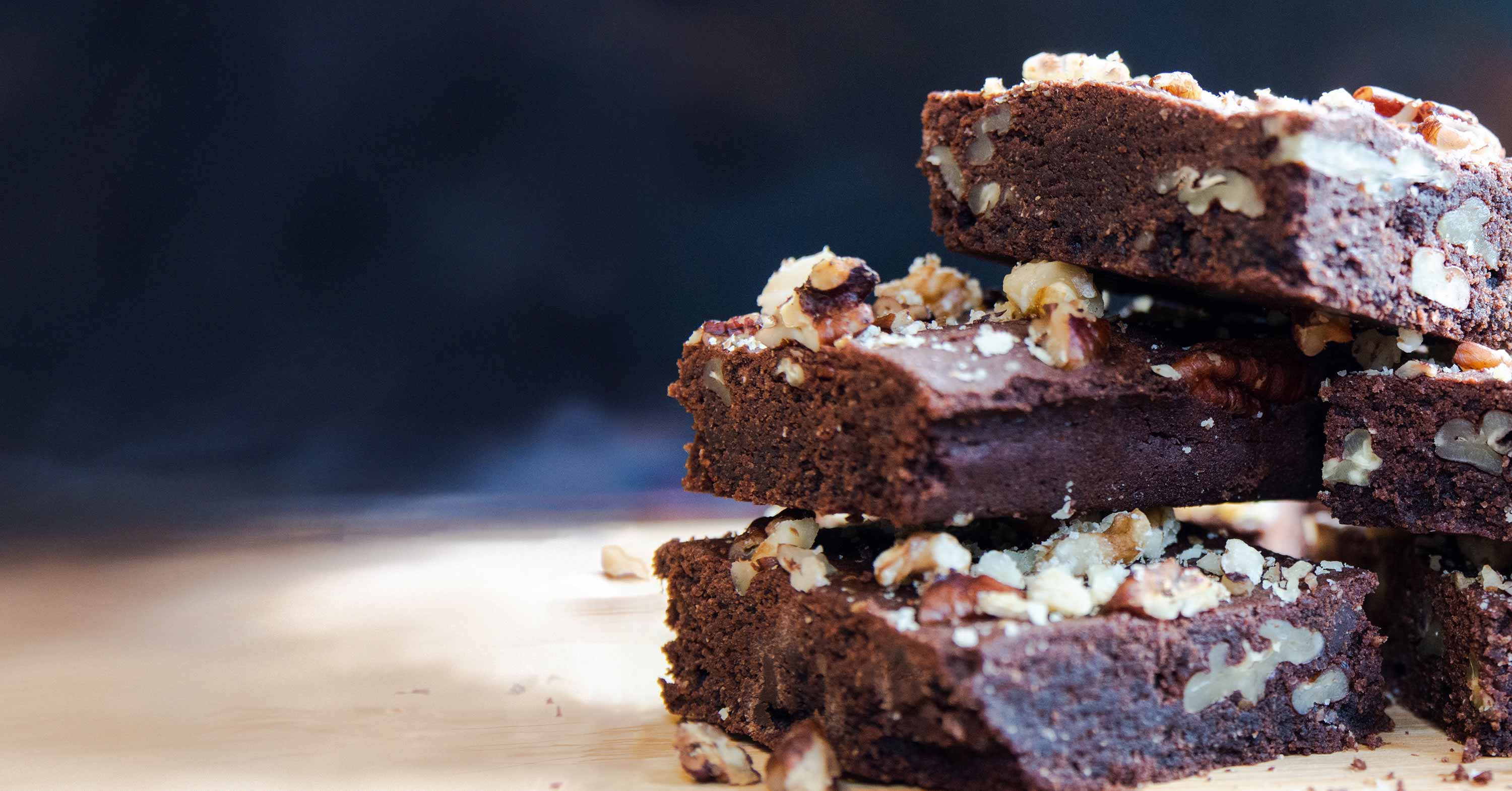 A stack of chocolate and pecan brownies, sprinkled with pecan crumbs and crushed walnut, fresh out of the oven